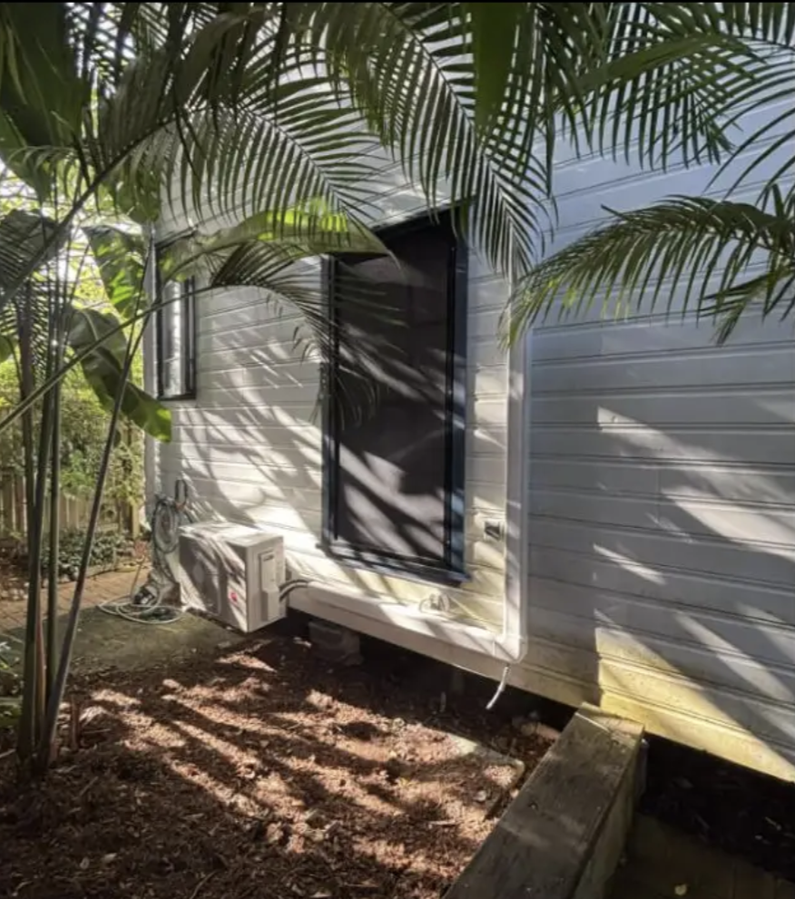 Split-system outdoor unit installed beside a weatherboard home surrounded by palms