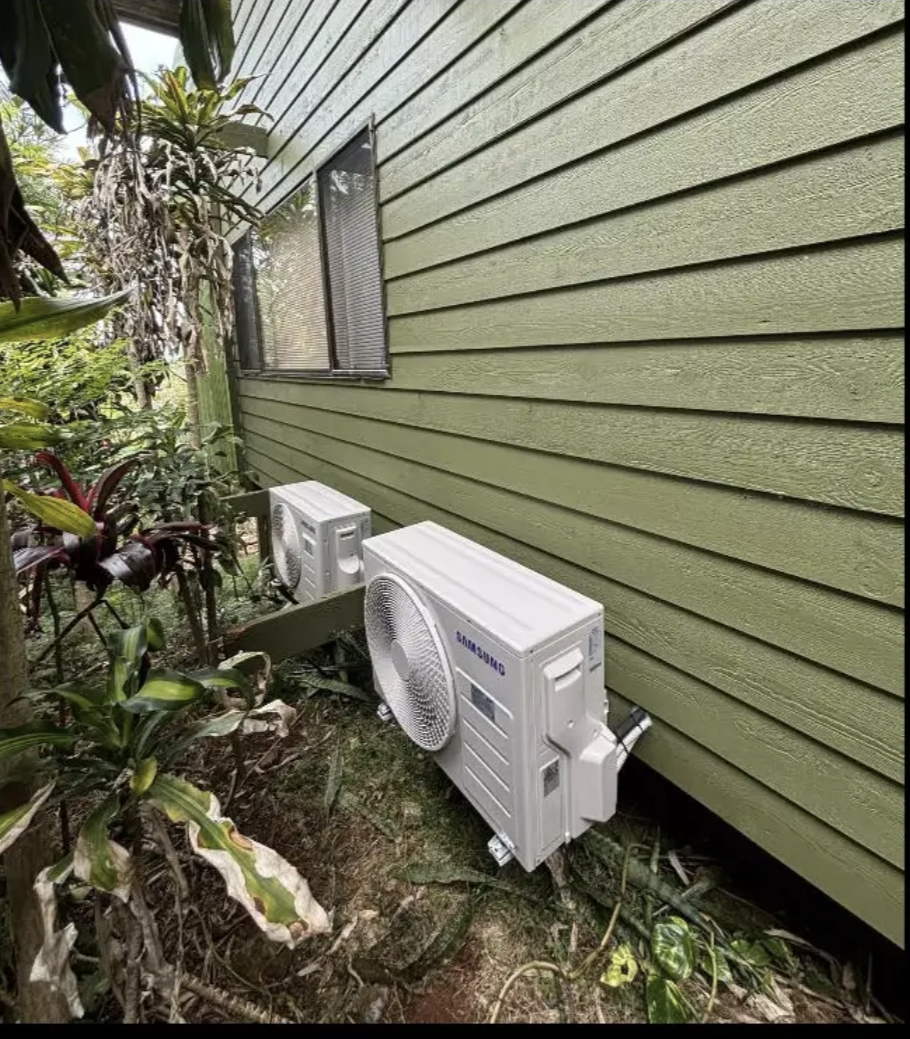 Two split-system outdoor units mounted on brackets against a green weatherboard wall